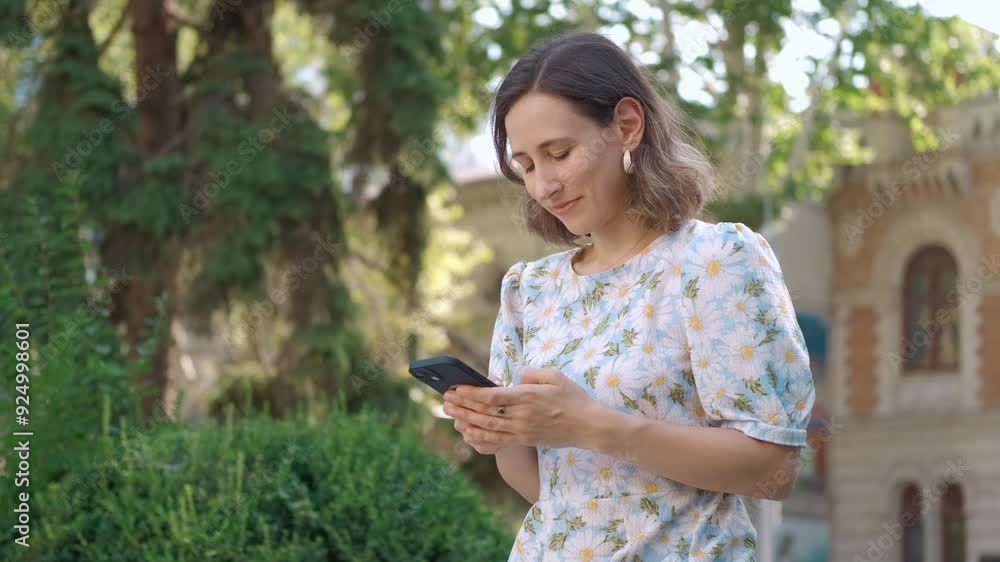 A young woman actively engages with her smartphone surrounded by lush greenery, showcasing modern lifestyle trends A young woman actively engages with her smartphone surrounded by lush greenery, showcasing modern lifestyle trends