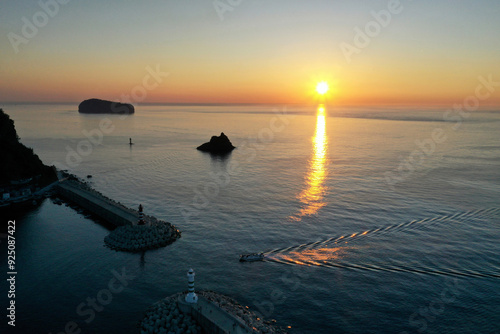 Jeodong-ri, Ulleung-gun, Gyeongsangbuk-do, South Korea - June 17, 2022: Aerial and sunrise view of a fishing boat sailing toward Jeodong Port against rising sun on the sea in summer photo