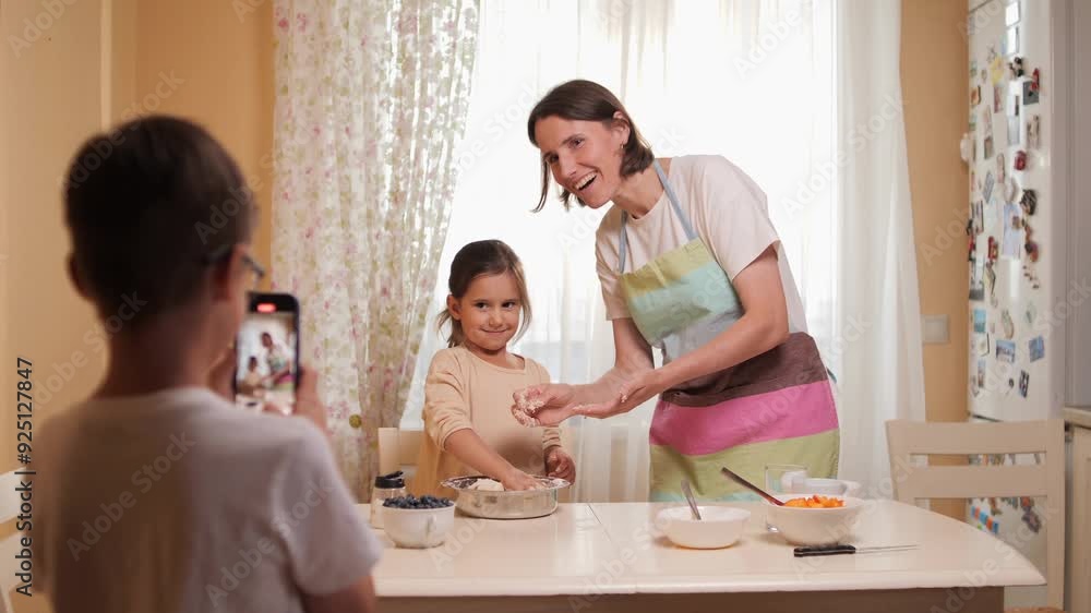 Parent teaching child cooking while sibling records with smartphone Parent teaching child cooking while sibling records with smartphone