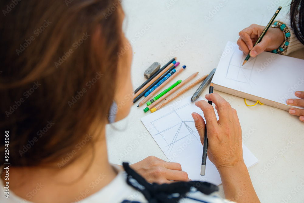 Top view, perspective of woman drawing on a table with notebook and colored pencils Top view, perspective of woman drawing on a table with notebook and colored pencils