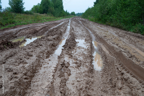 Messy rural dirt road after rain with puddles and deep tire tracks