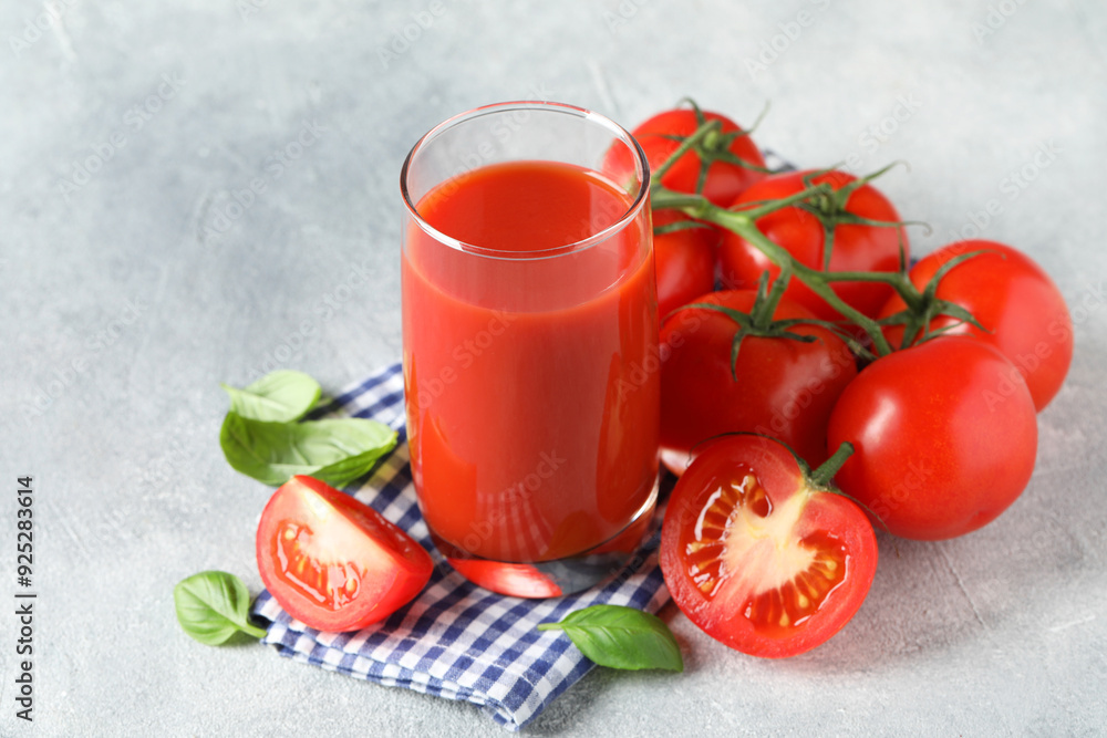 Tasty tomato juice in glass, basil leaves and fresh vegetables on grey textured table Tasty tomato juice in glass, basil leaves and fresh vegetables on grey textured table