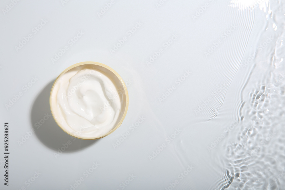 Cosmetic product. Jar with cream in water on light background, top view. Space for text