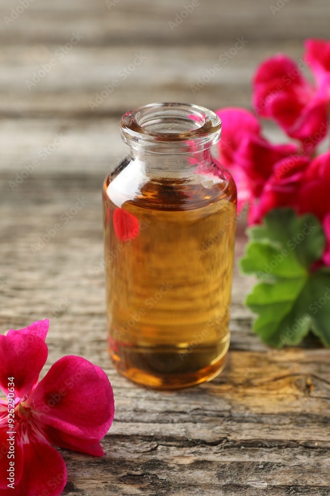 Bottle of geranium essential oil and beautiful flowers on wooden table, closeup Bottle of geranium essential oil and beautiful flowers on wooden table, closeup
