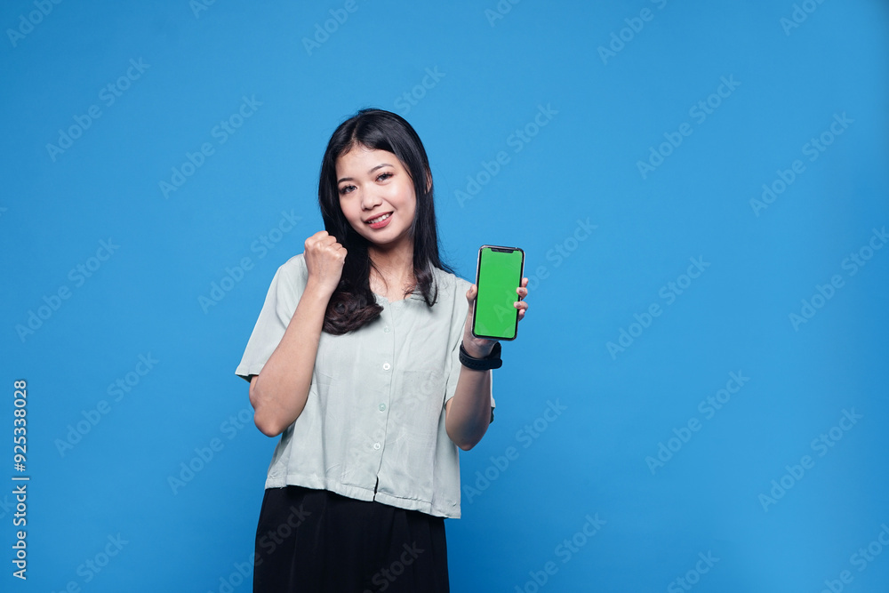 Young Asia lady shows empty smartphone screen with positive expression, smiles broadly, dressed in casual clothing feeling happiness on blue background Young Asia lady shows empty smartphone screen with positive expression, smiles broadly, dressed in casual clothing feeling happiness on blue background