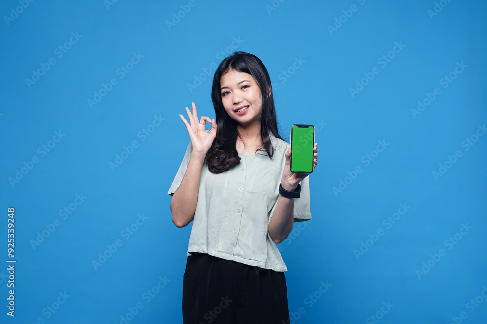 Beautiful Asian woman holding smartphone mockup of green screen and shows ok sign on blue background Beautiful Asian woman holding smartphone mockup of green screen and shows ok sign on blue background
