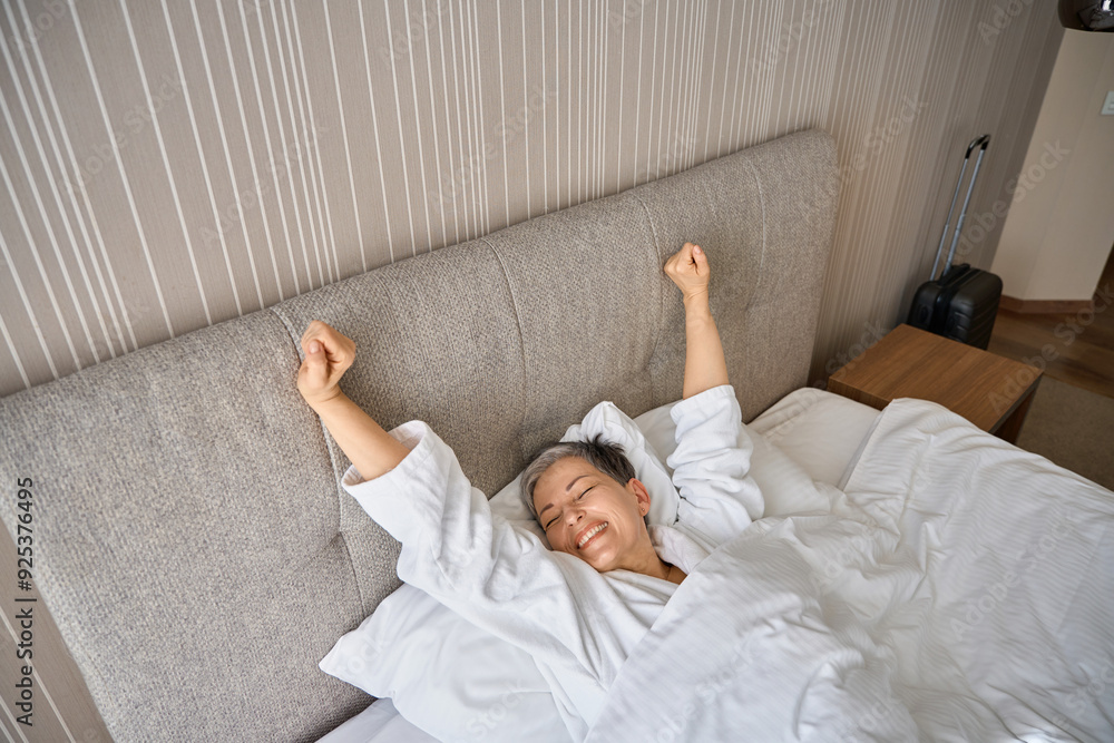 Beautiful woman waking up, stretching hands after good night sleep in hotel