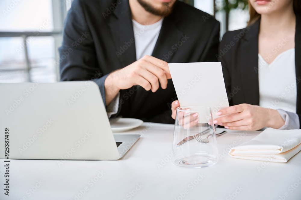Young man and woman using laptop during business meeting, holding menu Young man and woman using laptop during business meeting, holding menu