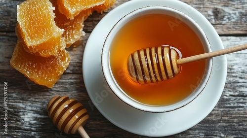 A cup of honey with a dipper on a wooden table. Honeycomb pieces next to the cup provide a rustic and natural touch.