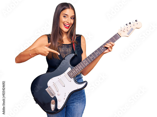 Young hispanic woman playing electric guitar smiling happy pointing with hand and finger