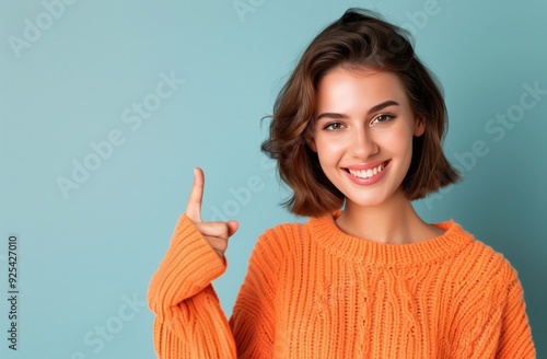 Young Woman Smiling While Pointing Up Against Blue Background in Cozy Orange ...
