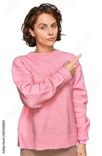 Young hispanic woman wearing casual clothes pointing with hand finger to the side showing advertisement, serious and calm face