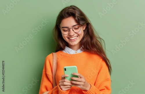 Young Woman Smiling While Texting on Her Phone Against a Mint Green Background