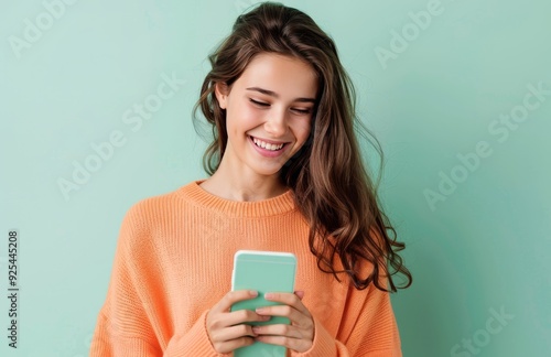Young Woman Smiling While Texting on Her Phone Against a Mint Green Background