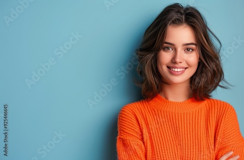 Young Woman Smiling While Pointing Up Against Blue Background in Cozy Orange ...