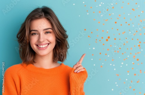 Young Woman Smiling While Pointing Up Against Blue Background in Cozy Orange ...