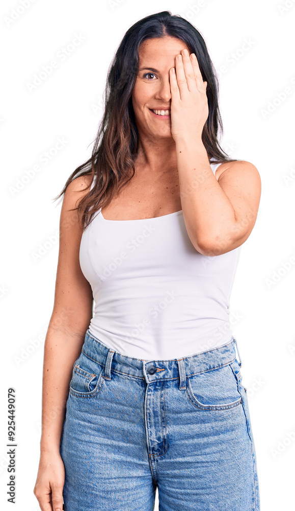 Young beautiful brunette woman wearing casual sleeveless t-shirt covering one eye with hand, confident smile on face and surprise emotion. Young beautiful brunette woman wearing casual sleeveless t-shirt covering one eye with hand, confident smile on face and surprise emotion.