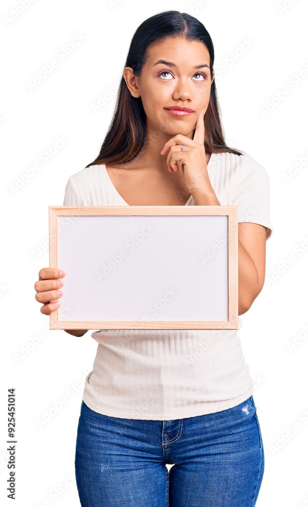 Young beautiful latin girl holding empty white chalkboard serious face thinking about question with hand on chin, thoughtful about confusing idea Young beautiful latin girl holding empty white chalkboard serious face thinking about question with hand on chin, thoughtful about confusing idea