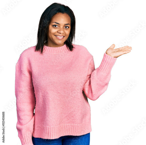 Beautiful hispanic woman wearing casual winter sweater smiling cheerful presenting and pointing with palm of hand looking at the camera.