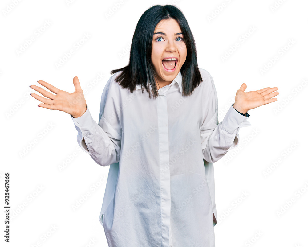 Young brunette woman with blue eyes wearing oversize white shirt celebrating crazy and amazed for success with arms raised and open eyes screaming excited. winner concept Young brunette woman with blue eyes wearing oversize white shirt celebrating crazy and amazed for success with arms raised and open eyes screaming excited. winner concept