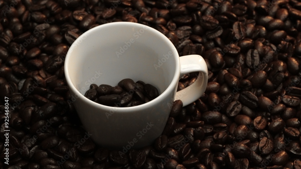 Close up of coffee bean falling in to coffee cup surrounded by pile of beans. Dropping aromatic blending bean in to white cup. Top view of coffee drop in to glass with black background. Comestible. Close up of coffee bean falling in to coffee cup surrounded by pile of beans. Dropping aromatic blending bean in to white cup. Top view of coffee drop in to glass with black background. Comestible.
