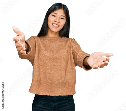 Beautiful young asian woman wearing casual winter sweater looking at the camera smiling with open arms for hug. cheerful expression embracing happiness.