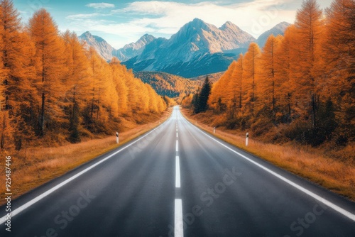A serene road leading through picturesque autumn trees toward majestic mountains under a blue sky.