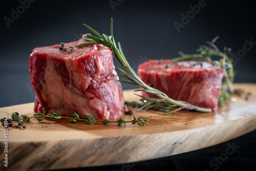 Raw Filet Mignon on a cutting board with rosemary and black pepper.