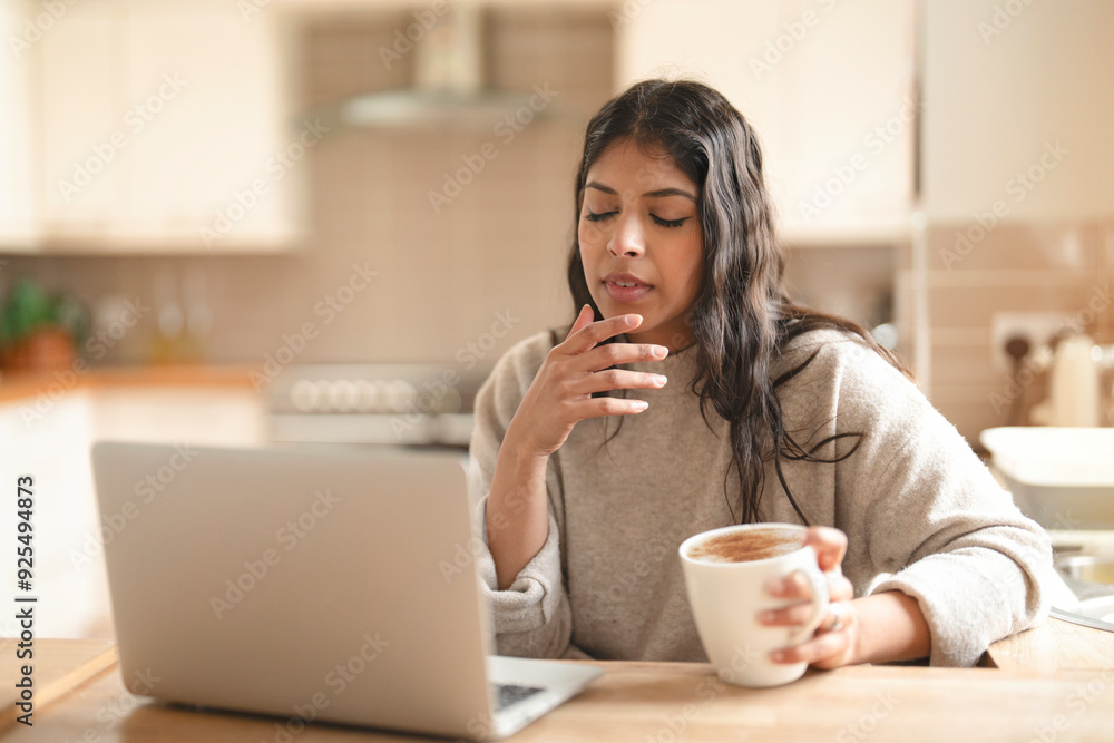 Young Woman Enjoying Coffee While Working on Laptop in Cozy Kitchen Young Woman Enjoying Coffee While Working on Laptop in Cozy Kitchen