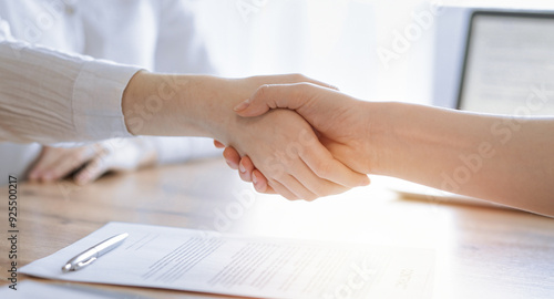 Business people shaking hands above contract papers just signed on the wooden table, close up. Lawyers at meeting. Teamwork, partnership, success concept