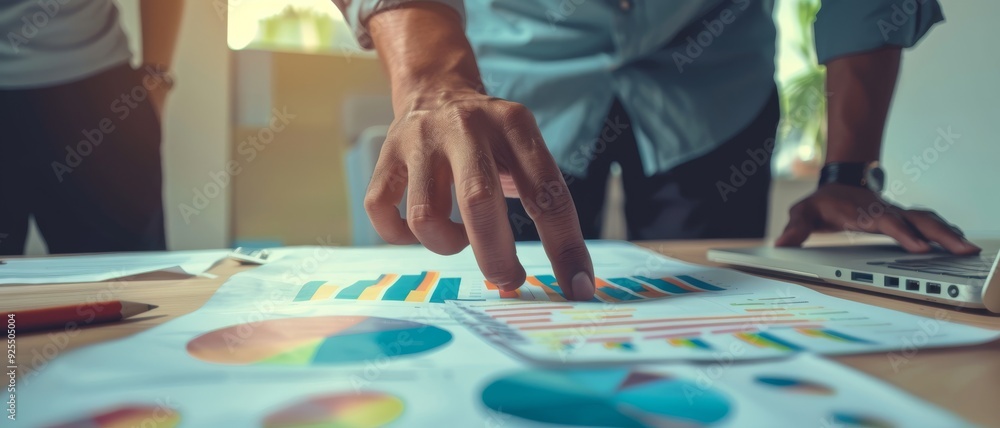 Obraz premium Professionals analyzing and pointing at colorful charts on a desk, showing collaboration and data interpretation.