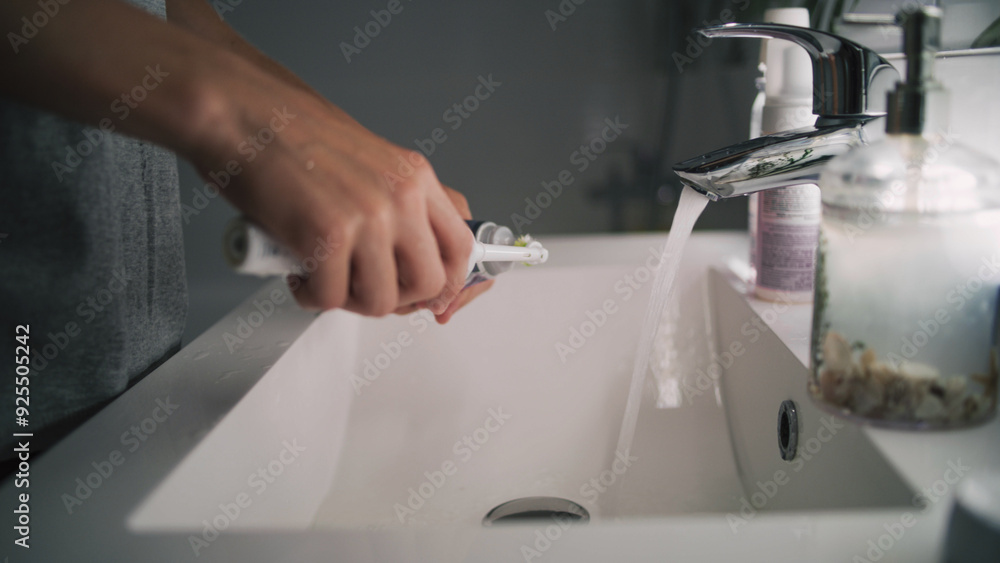 Caucasian boy looks at mirror in bathroom, brushes his teeth. Teenager stands in front of sink and uses electrical toothbrush before bedtime. Evening bath routine. Lifestyle concept. Low angle shot. Caucasian boy looks at mirror in bathroom, brushes his teeth. Teenager stands in front of sink and uses electrical toothbrush before bedtime. Evening bath routine. Lifestyle concept. Low angle shot.