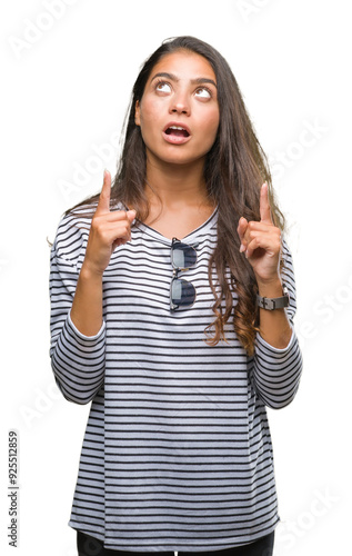 Young beautiful arab woman wearing sunglasses over isolated background amazed and surprised looking up and pointing with fingers and raised arms. photo