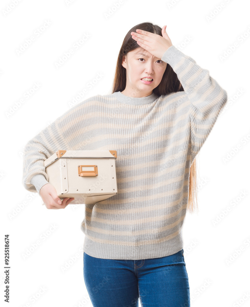 Young Chinese woman over isolated background holding a box stressed with hand on head, shocked with shame and surprise face, angry and frustrated. Fear and upset for mistake. Young Chinese woman over isolated background holding a box stressed with hand on head, shocked with shame and surprise face, angry and frustrated. Fear and upset for mistake.