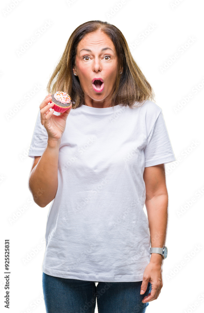 Middle age hispanic woman eating cupcake over isolated background scared in shock with a surprise face, afraid and excited with fear expression