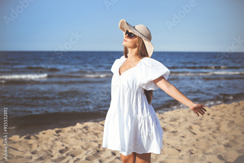 Happy blonde woman is on the ocean beach in a white dress and sunglasses, open arms