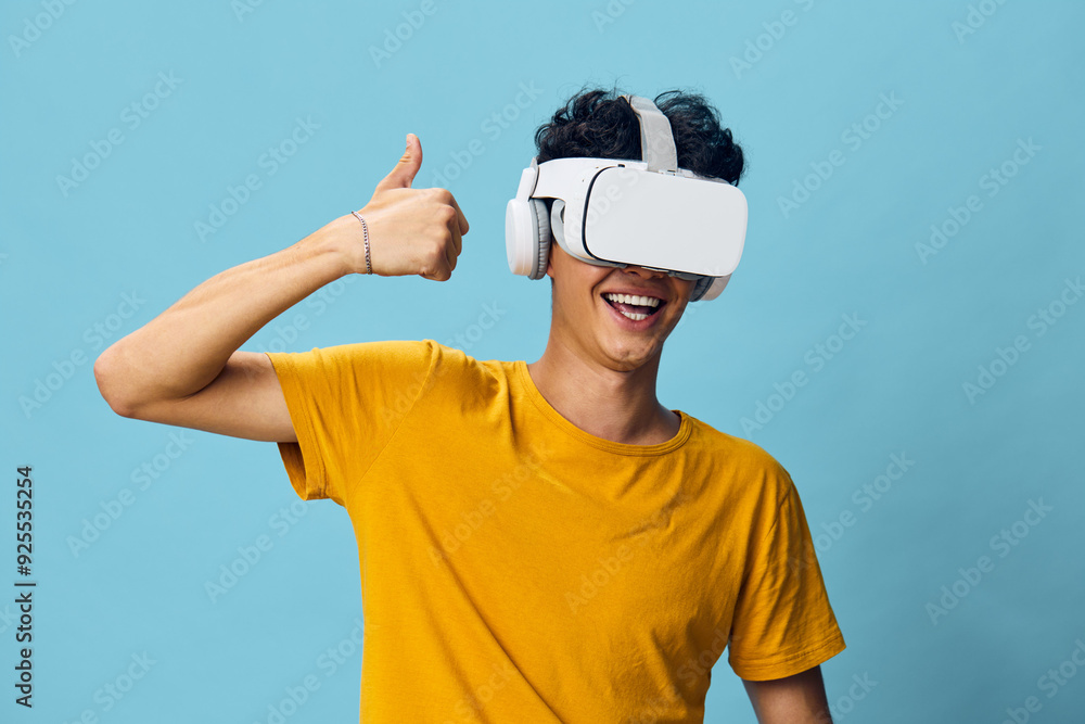 virtual reality, VR headset, happy young man, thumbs up, blue background, youth technology, gaming excitement, modern lifestyle, immersive experience, joy expression, smiling face, casual wear