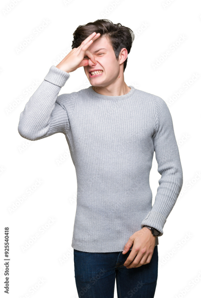Young handsome man wearing winter sweater over isolated background smelling something stinky and disgusting, intolerable smell, holding breath with fingers on nose. Bad smells concept. Young handsome man wearing winter sweater over isolated background smelling something stinky and disgusting, intolerable smell, holding breath with fingers on nose. Bad smells concept.