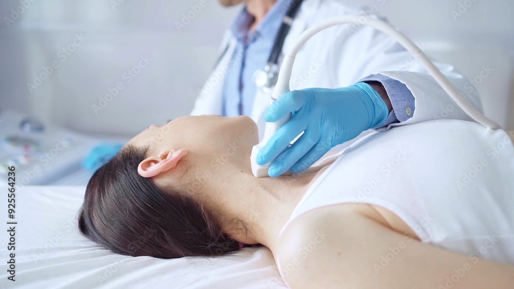 Doctor man wearing blue medical gloves is using ultrasound equipment on neck of female patient lying down for a medical examination Doctor man wearing blue medical gloves is using ultrasound equipment on neck of female patient lying down for a medical examination