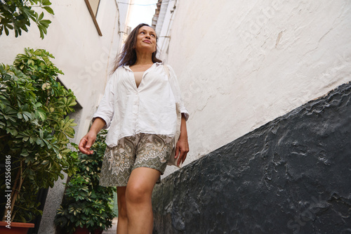 Confident woman walking along a narrow alleyway, wearing a casual white shirt and patterned shorts, exuding a sense of freedom and joy photo