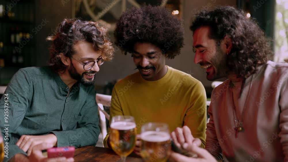 Three happy multiracial friends using mobile phone sitting on table at bar. Technology and male friendship concept. Three happy multiracial friends using mobile phone sitting on table at bar. Technology and male friendship concept.