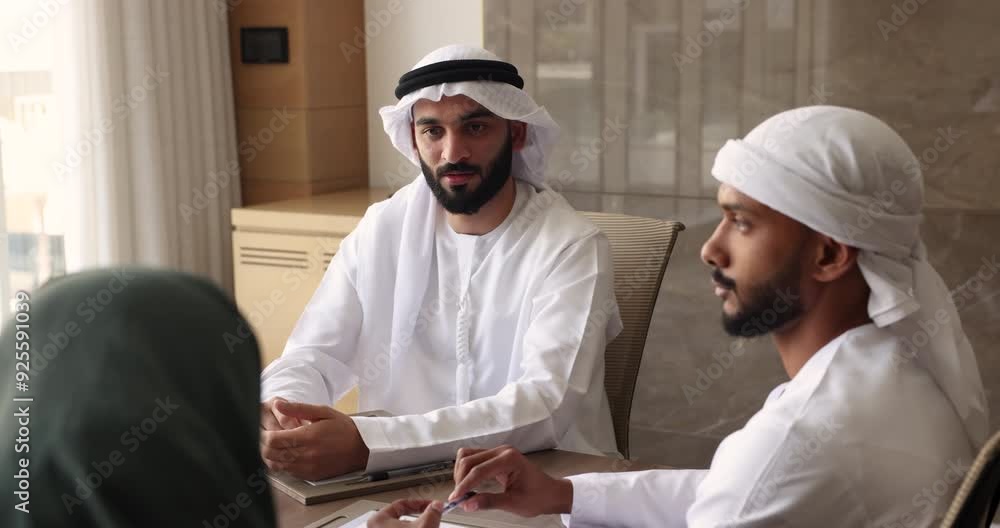 Young male Arab boss talking to employees in Muslim clothes, sitting at ...