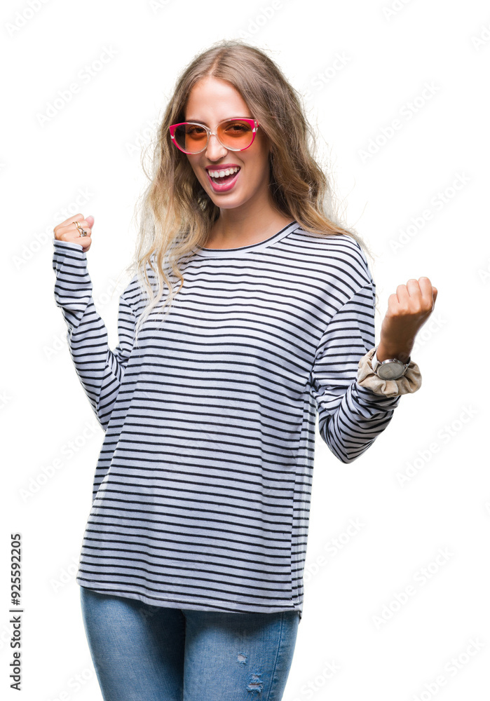 Beautiful young blonde woman wearing sunglasses over isolated background very happy and excited doing winner gesture with arms raised, smiling and screaming for success. Celebration concept. Beautiful young blonde woman wearing sunglasses over isolated background very happy and excited doing winner gesture with arms raised, smiling and screaming for success. Celebration concept.