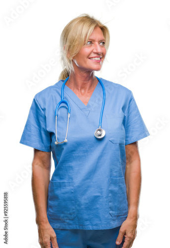 Middle age blonde nurse surgeon doctor woman over isolated background looking away to side with smile on face, natural expression. Laughing confident.