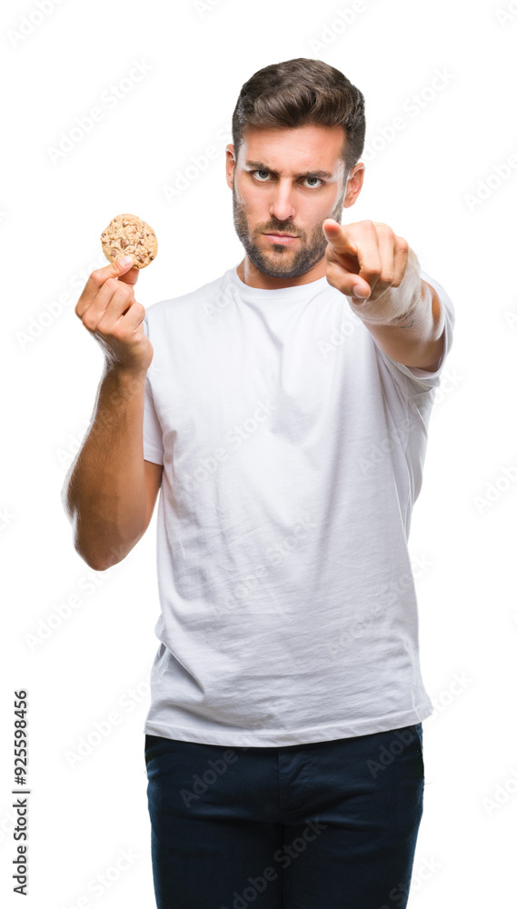 Young handsome man eating chocolate chips cookie over isolated background pointing with finger to the camera and to you, hand sign, positive and confident gesture from the front Young handsome man eating chocolate chips cookie over isolated background pointing with finger to the camera and to you, hand sign, positive and confident gesture from the front