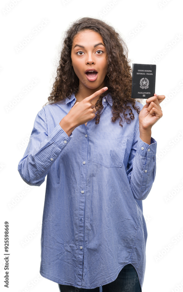 Young hispanic woman holding passport of Italy very happy pointing with hand and finger Young hispanic woman holding passport of Italy very happy pointing with hand and finger