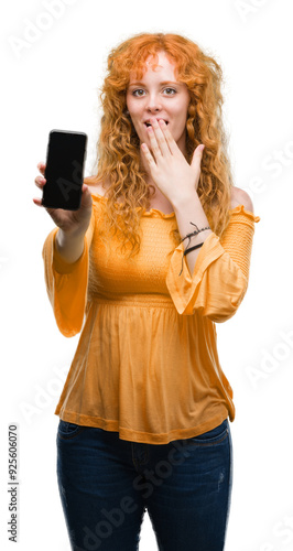 Young redhead woman showing smartphone cover mouth with hand shocked with shame for mistake, expression of fear, scared in silence, secret concept