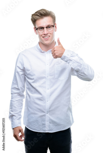 Young handsome blond man doing happy thumbs up gesture with hand. Approving expression looking at the camera with showing success.