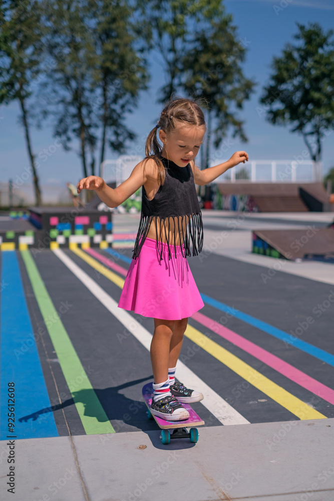 A preschool-age girl rides a skateboard in a skate park on a sunny summer day A preschool-age girl rides a skateboard in a skate park on a sunny summer day