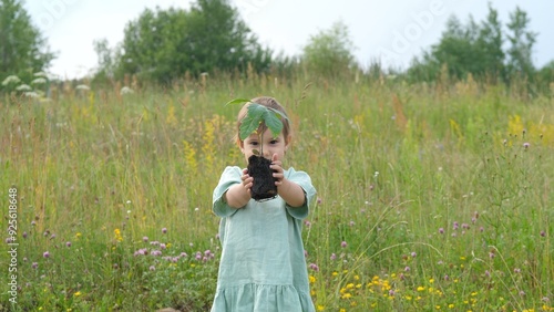 Little girl holding oak tree sapling in field